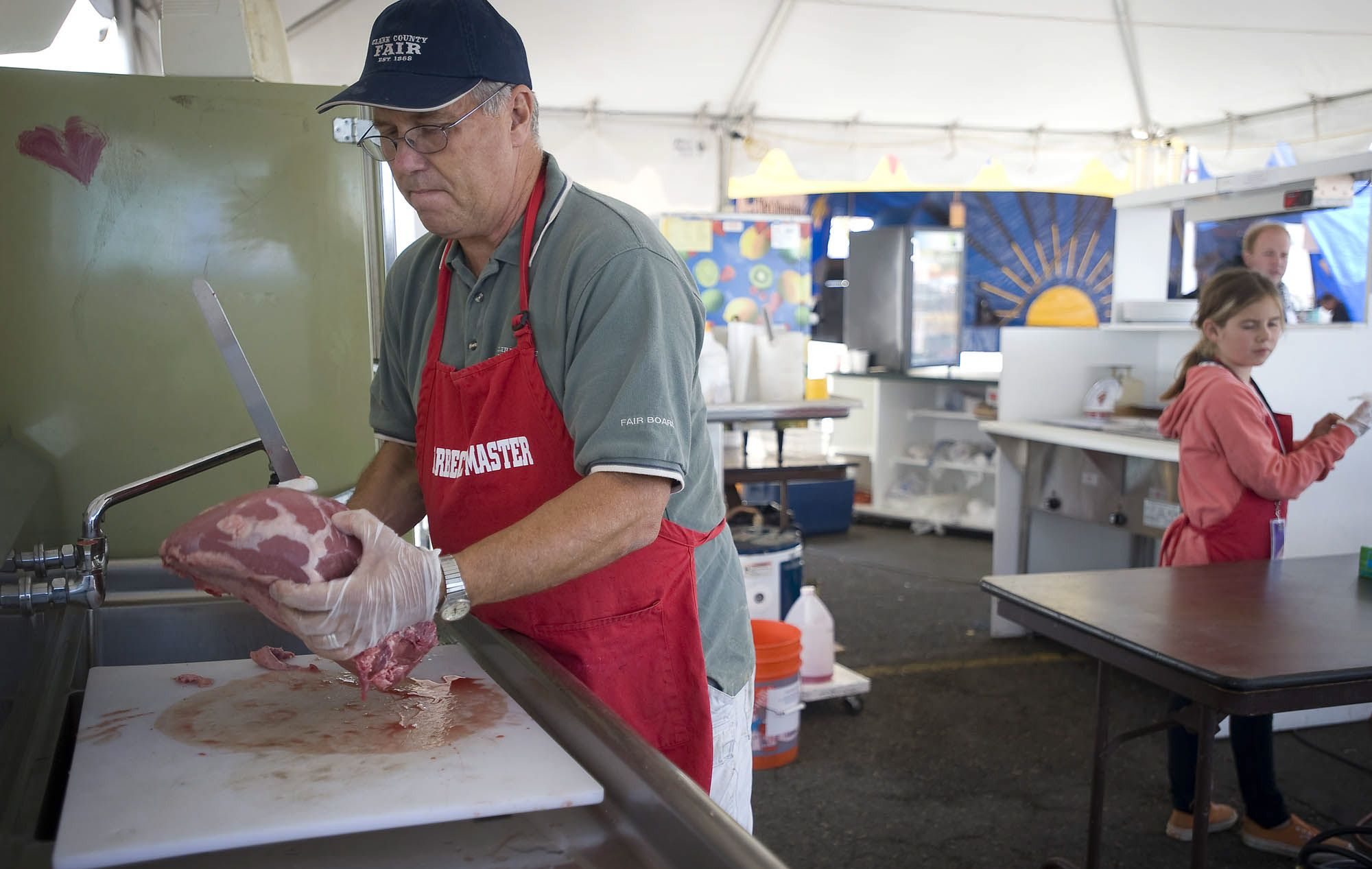 Clark County Commissioner Marc Boldt prepares beef bottom round roasts for the coals Thursday in the Young Life booth at the Clark County Fair. Also working the booth is his daughter Molly, 10.