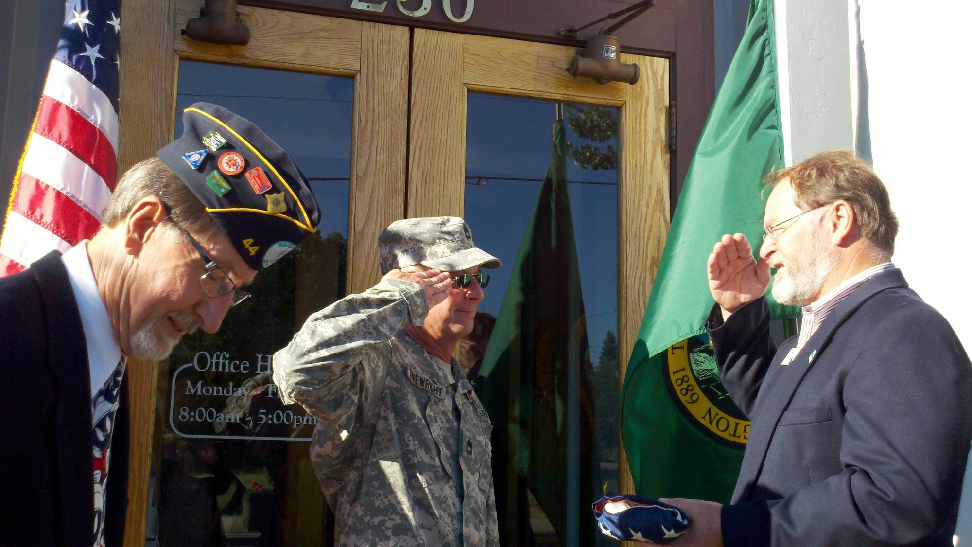 Army Sgt. 1st Class David Sivewright, center, presents the flag he carried more than 2,000 miles to Ridgefield City Councilman Darren Wertz, right, on the steps of Ridgefield City Hall.