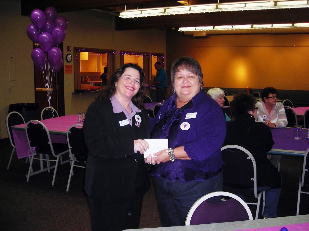 Michelle Bart, president of Soroptimist International of Southwest Washington, presents a contribution to Debra Adams, director of YWCA SafeChoice, during the Purple Lights Bingo event.
