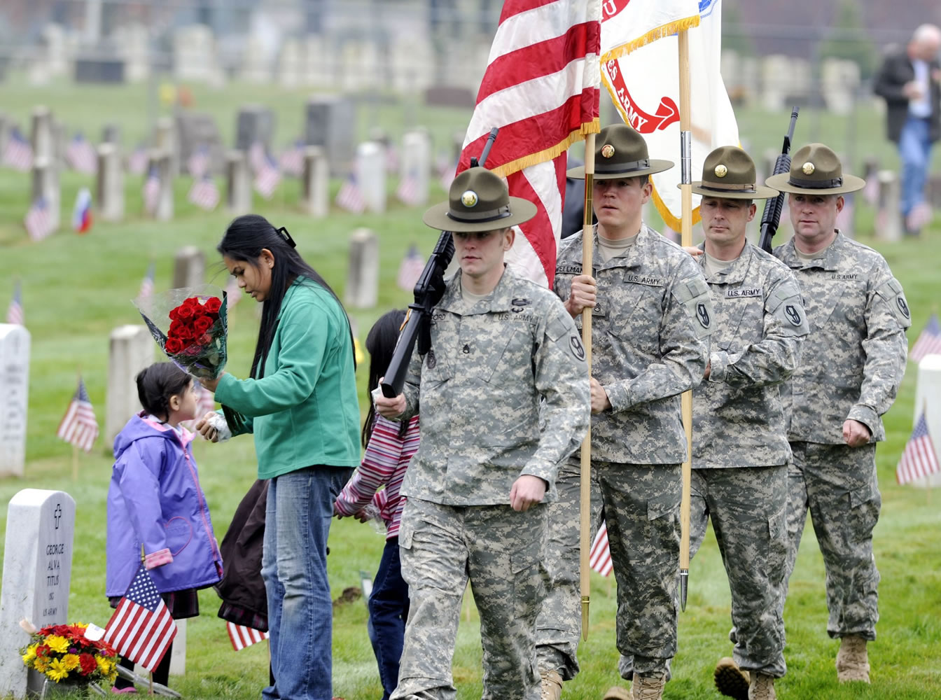 Family members leave flowers at the grave of George Titus as soldiers from the 2nd Brigade, 95th Division, rehearse posting the colors prior to Friday's Veterans Day observance at the Vancouver Barracks Post Cemetery.