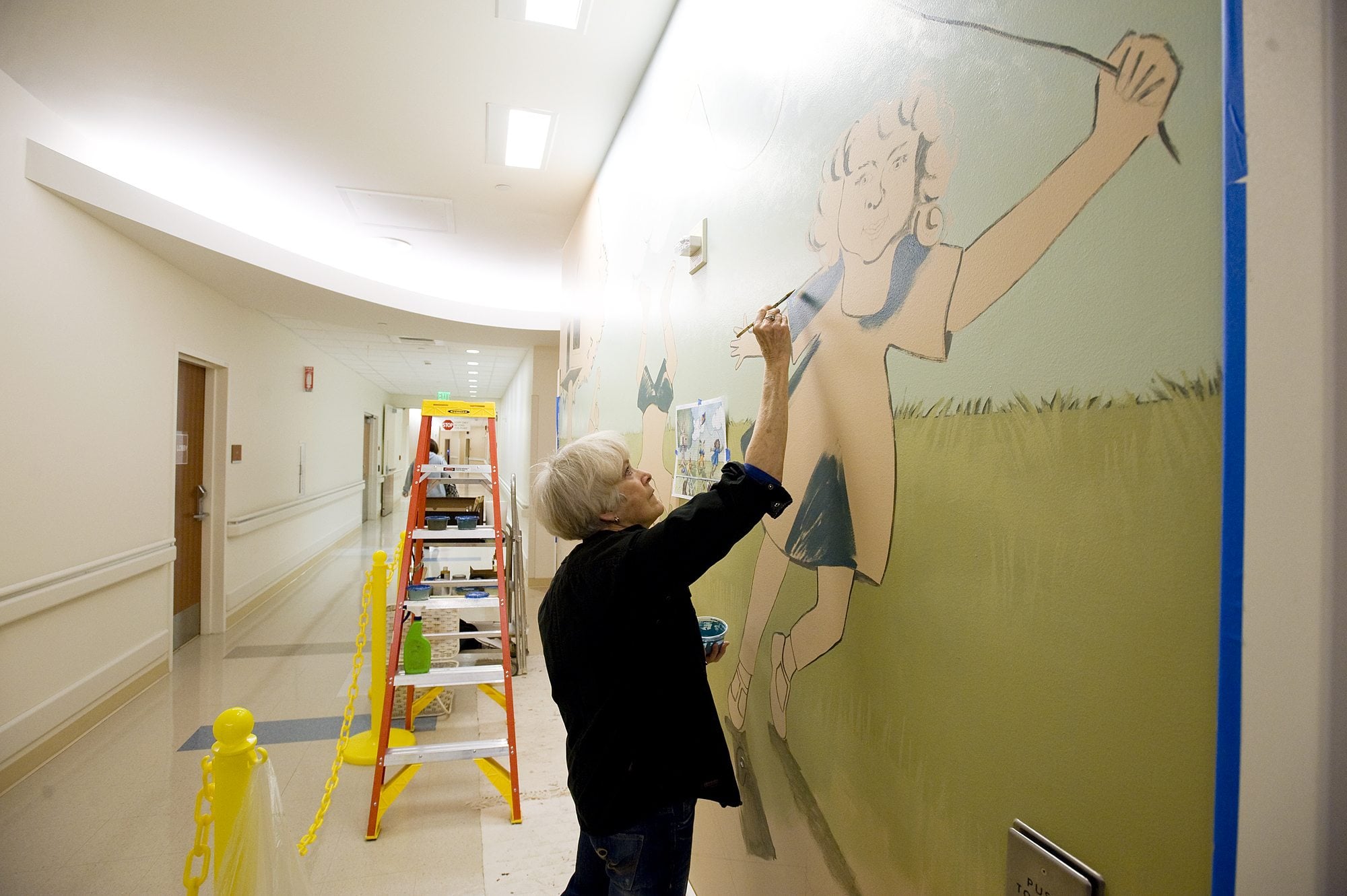 Retired art teacher Rebecca Anstine paints a mural Thursday at the entrance of the pediatric emergency department at Legacy Salmon Creek Medical Center.
