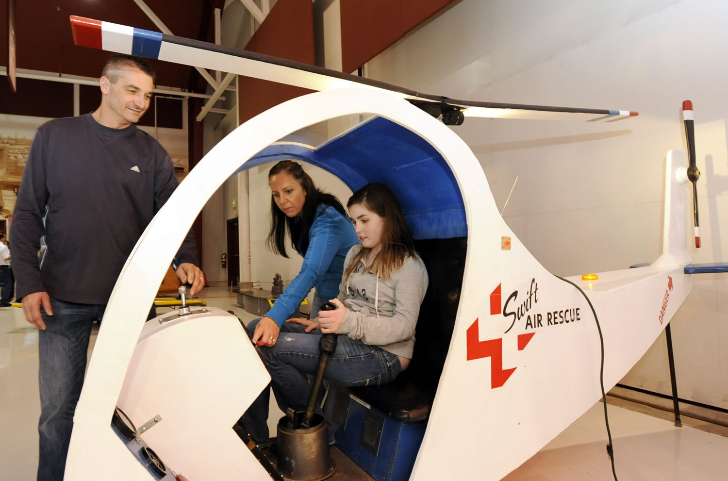Victoria Quintero, seated, with her parents Tanya Quintero and Jaider Quintero, left, examines a hands-on helicopter display at Pearson Air Museum.