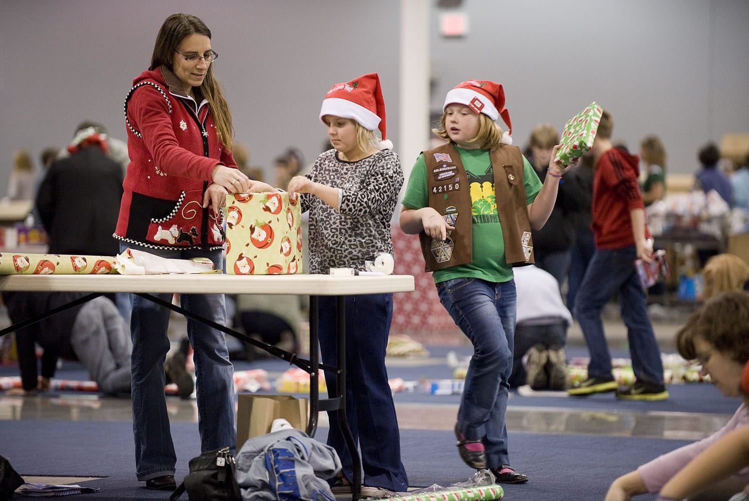 Volunteers, from left, Debbie LaPier, Delainey Phelps, 8, and Sophia Davis, 8, both from Girl Scout Brownie Pack 42150, wrap presents for needy families, Thursday, December 15, 2011.