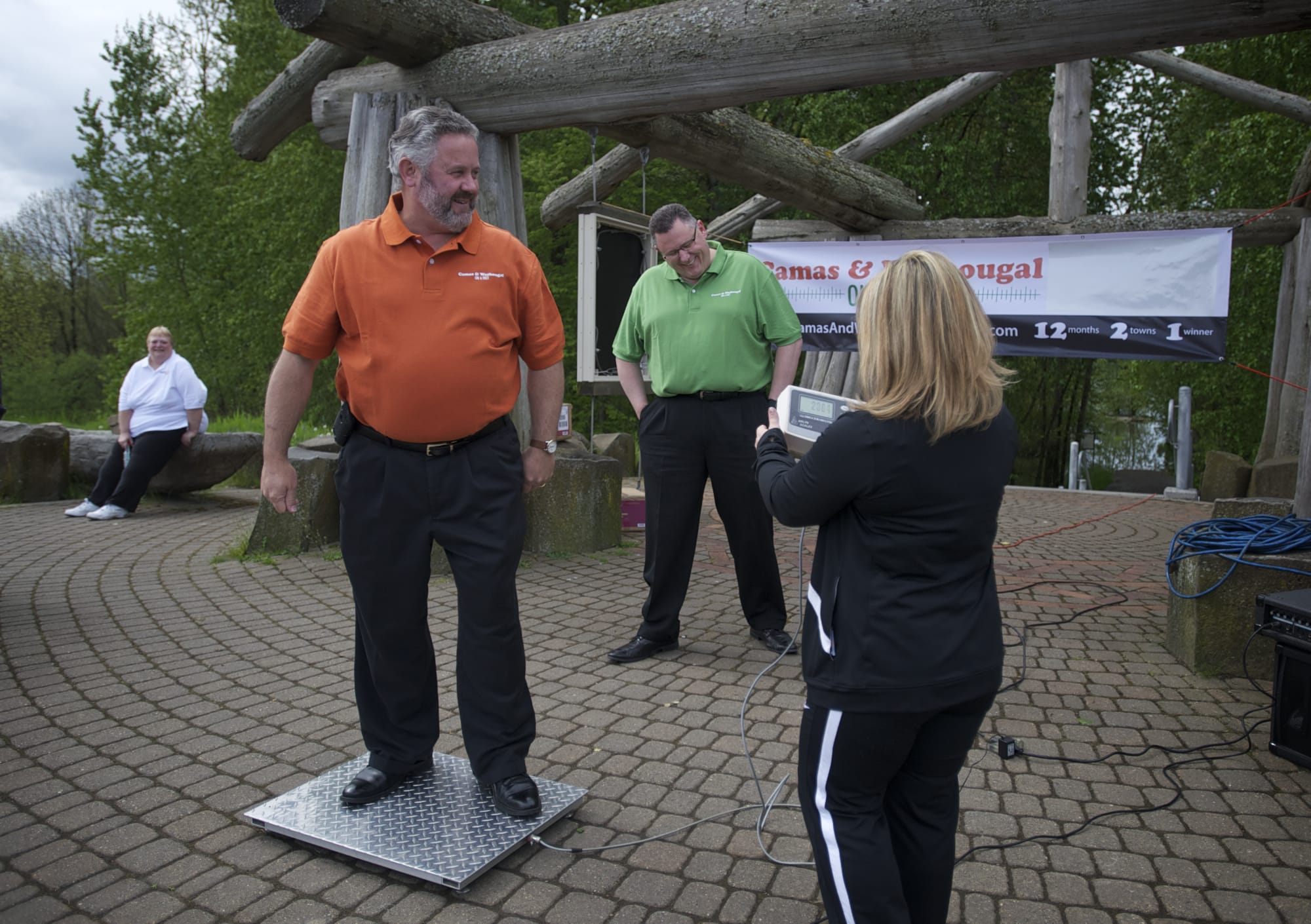 Washougal Mayor Sean Guard, in orange shirt, steps on the scale as Camas Mayor Scott Higgins, in green shirt, watches during the launch of the community weight-loss challenge, &quot;Camas and Washougal On A Diet,&quot; on Wednesday at Capt. William Clark Park in Washougal.