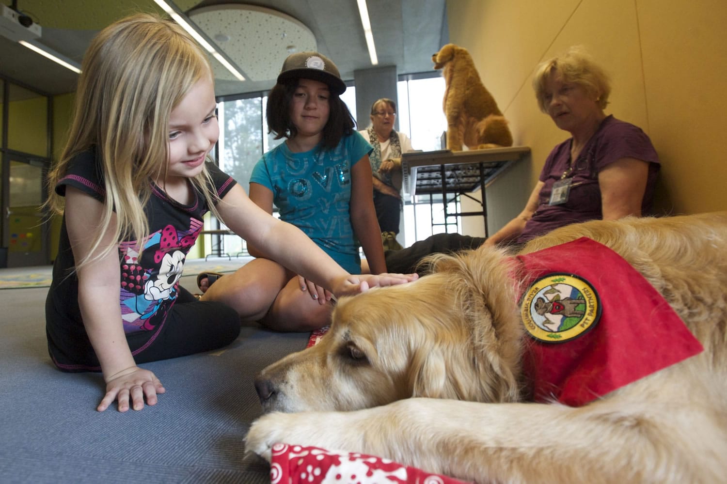 Lola Fuller, 6, left, and Sofia Arellano, 9, meets Columbia River Pet Partners therapy dog Crunch, a golden retriever. The children practiced their reading skills by reading to him at the Vancouver Community Library on Aug. 13, 2014. Therapy animal handler Michael Kay Richardson watches at rear.