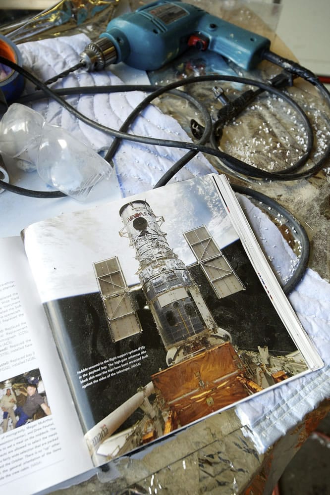 A magazine with a photograph of the real Hubble Space Telescope sits on a workbench for reference at Masterpiece Models.