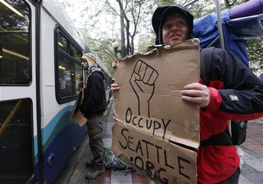 Dustin Noah, right, stands with another protester who stands within inches of a passing bus Thursday morning, Oct. 6, 2011, in Seattle's Westlake Park. About 50 people remained in the park Thursday morning, without tents, following the arrests of 25 people there Wednesday. Police moved in Wednesday after demonstrators refused to remove tents, which are not allowed in city parks.