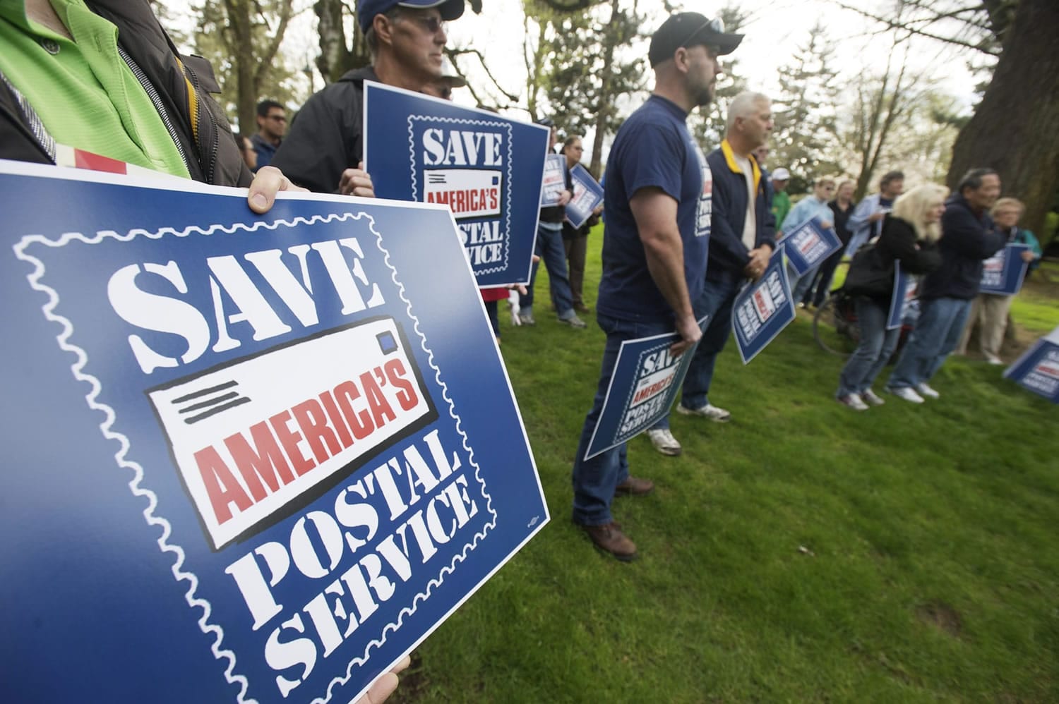 Letter carriers and members of the public hold signs on Thursday on Officers Row during a demonstration to protest changes to the U.S.