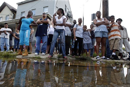 A crowd watches from a street corner Wednesday, Aug. 31, 2011, in Paterson, N.J., as New Jersey Gov. Chris Christie and Department of Homeland Security Secretary Janet Napolitano make a stop on a tour of areas flooded by Hurricane Irene. Later it was announced to the crowd that President Obama had signed a disaster declaration for hard-hit New Jersey after Hurricane Irene left much of northern New Jersey flooded.