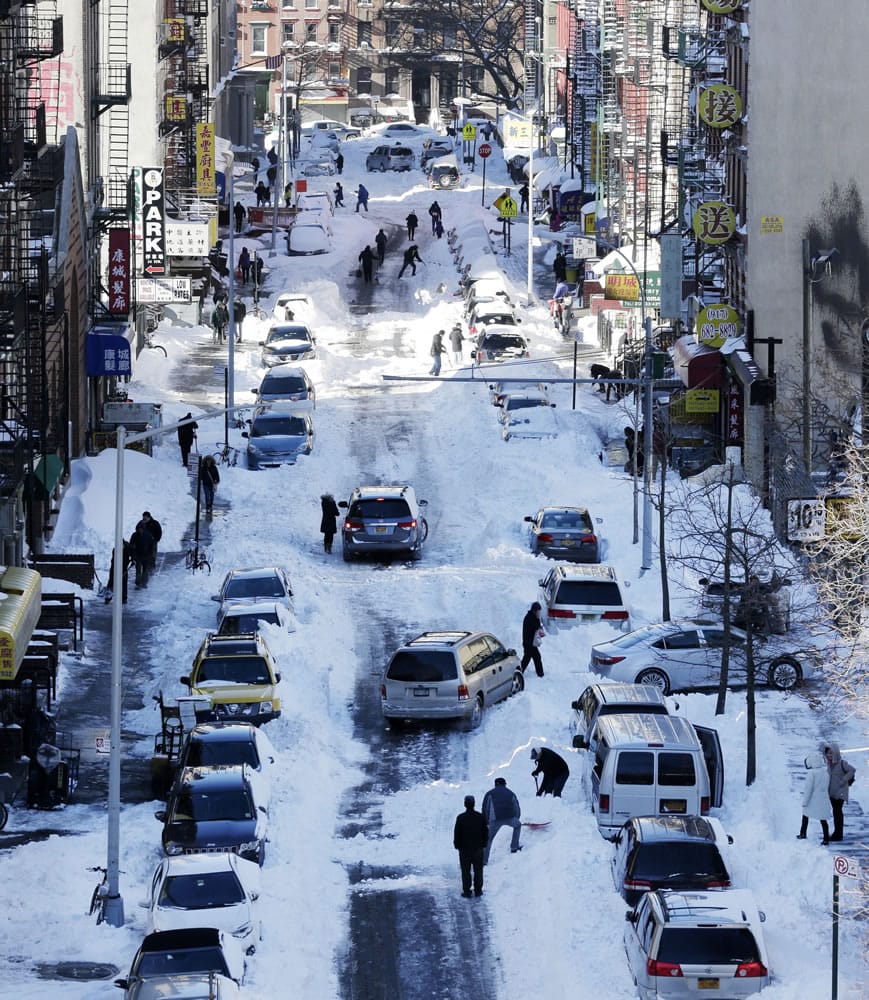 People clear snow from parked cars in the Chinatown neighborhood in New York on Sunday, when millions of Americans began digging out from a mammoth blizzard.