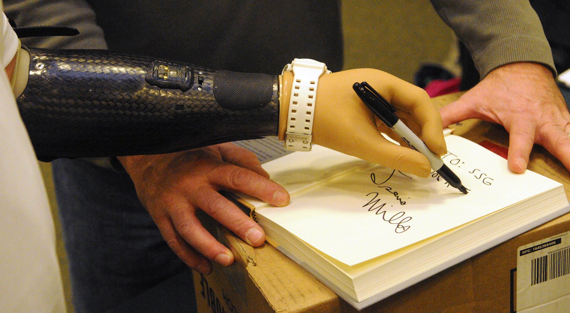Travis Mills autographs a copy of his book &quot;Tough As They Come&quot; with his left prosthetic hand last month at a Barnes and Noble store in Augusta, Maine.