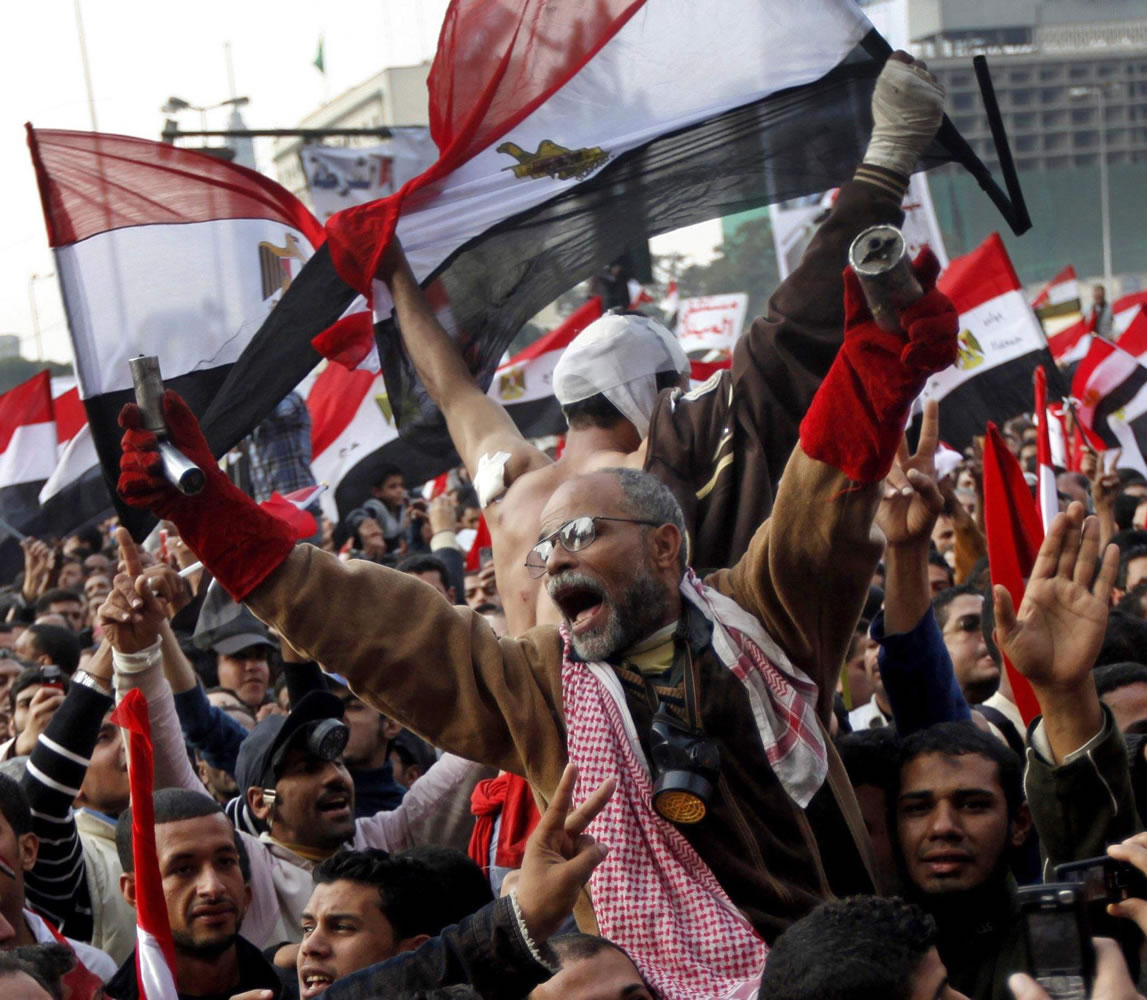 Protesters, including a man holding tear-gas canisters, chant slogans and wave national flags during a rally Friday in Tahrir Square in Cairo, Egypt.