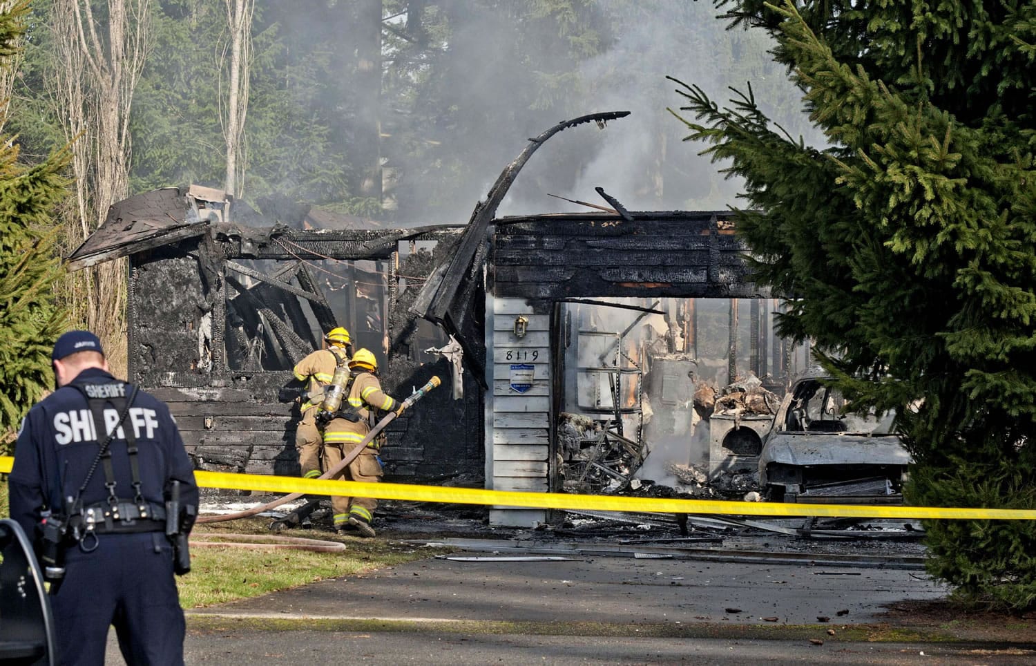 A Pierce County Sheriff's deputy and Graham Firefighters work around the smoldering remains of a house near Fredrickson Sunday, where, according to a sheriff's spokesman, three bodies were were found. The bodies are believed to be Josh Powell and his two sons.