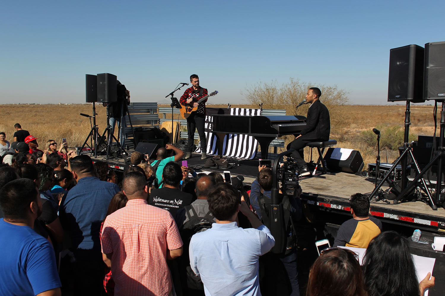 John Legend, right, and Colombian rock star Juanes perform over a flat bed truck platform in front of a detention center in Eloy, Ariz., on Wednesday. The artists performed in front of some 250 people in protest against massive migrant deportations as part of the Legends&#039; campaign #FREEAMERICA.