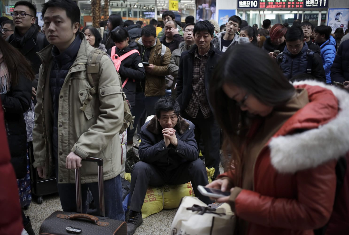 A man, center, sits on his belonging as he waits with other Chinese travelers to board a train Sunday at the south train station in Beijing. Chinese are packing train and bus stations as the peak travel season kicks into high gear this weekend with hundreds of millions of people going home for Spring Festival celebrations -- or heading for vacation destinations.
