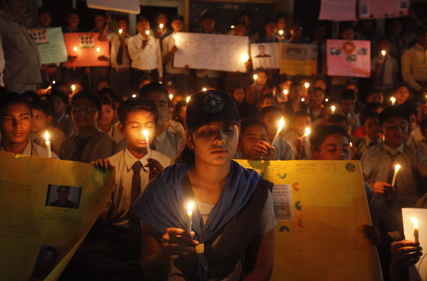 Indian students hold candles and placards as they pay tribute to the Indian soldiers killed in the Pathankot air base attack, at a school in Ahmadabad, India, Tuesday, Jan. 5, 2016.
