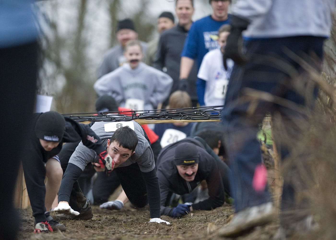 Participants go underneath an obstacle during the March Muddy Madness race that puts runners through a cross country course filled with mud, both natural and man-made obstacles and blackberry bushes on a farm in Felida.