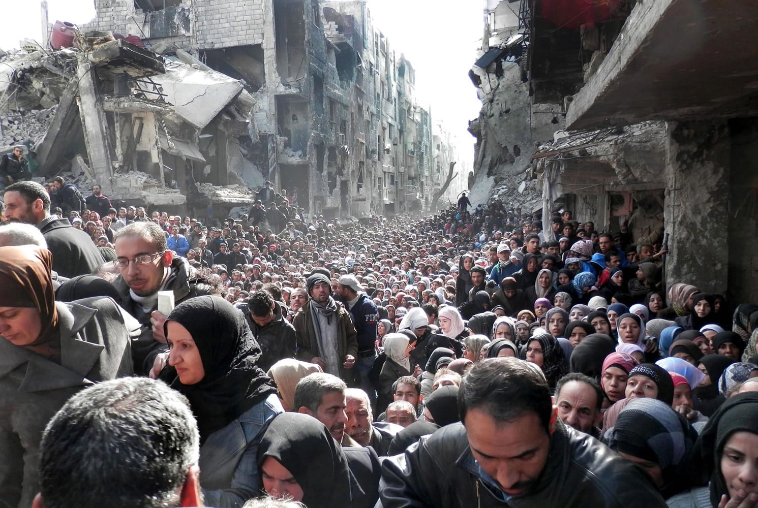 FILE - In this Jan. 31, 2014 file photo released by the United Nations Relief and Works Agency for Palestine Refugees in the Near East (UNRWA), shows residents of the besieged Palestinian camp of Yarmouk, queuing to receive food supplies, in Damascus, Syria. That year, the U.N.