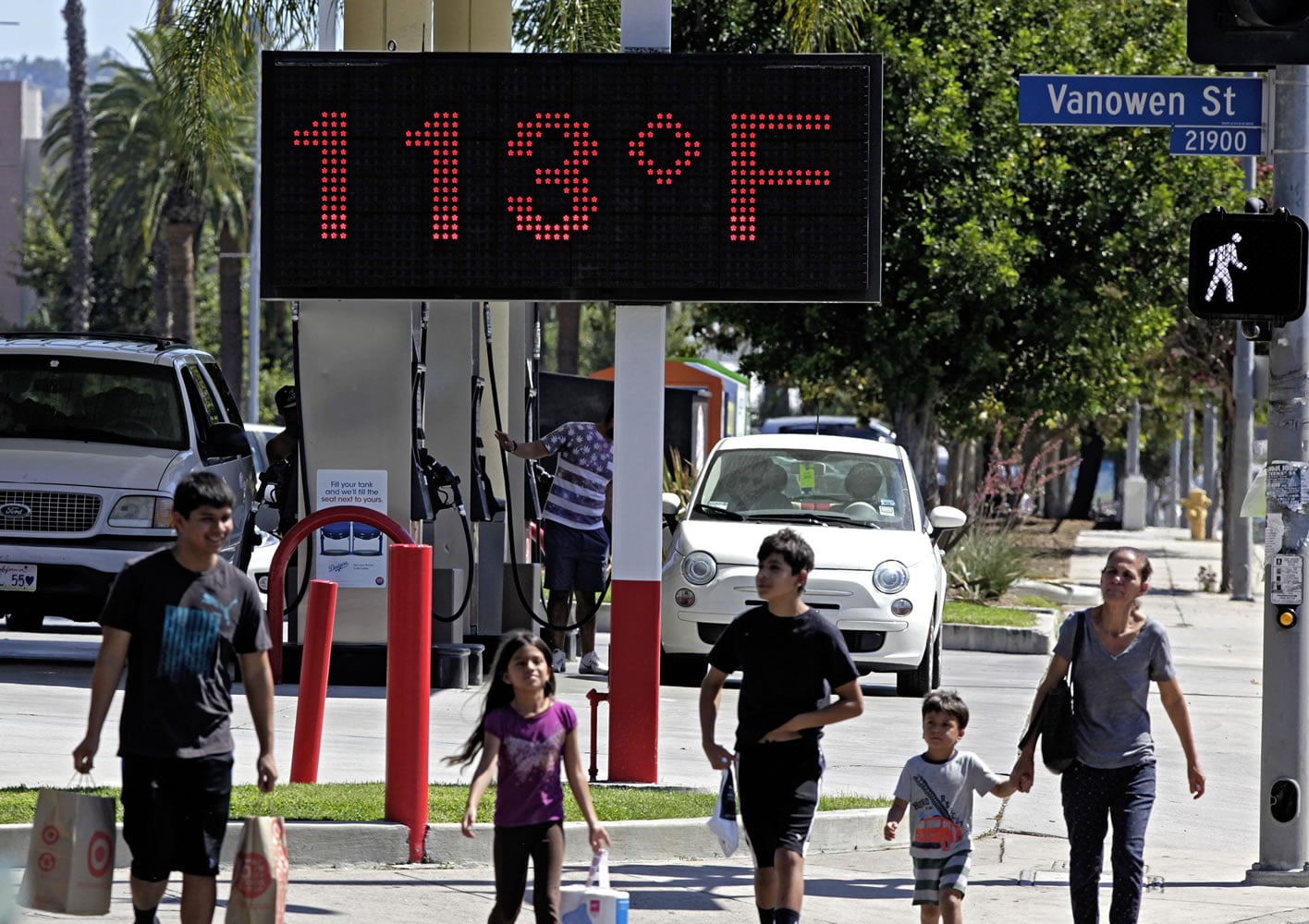 Pedestrians walk past a digital thermometer reading 113 degrees Fahrenheit in the Canoga Park section of Los Angeles.