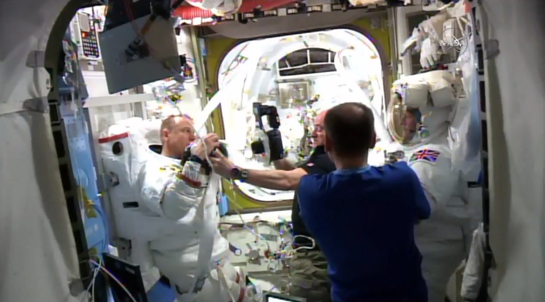 Astronaut Scott Kelly, center background, photographs parts of Timothy Kopra&#039;s space suit after a spacewalk with British spaceman Timothy Peake, right, was cut short after water leaked into Kopra&#039;s helmet.