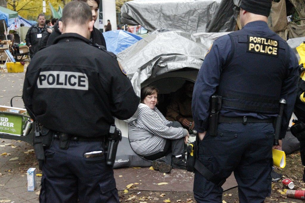 Erin Robertson, sits in the doorway of a tent while Portland Police look on at the Occupy Portland encampment Friday in Portland. Mayor Sam Adams has ordered one of the largest Occupy Wall Street camps in the country to pull up stakes. The protesters and homeless people at Occupy Oregon are trying to figure out what's next as they face a Saturday deadline for leaving two downtown park blocks they've occupied since Oct.