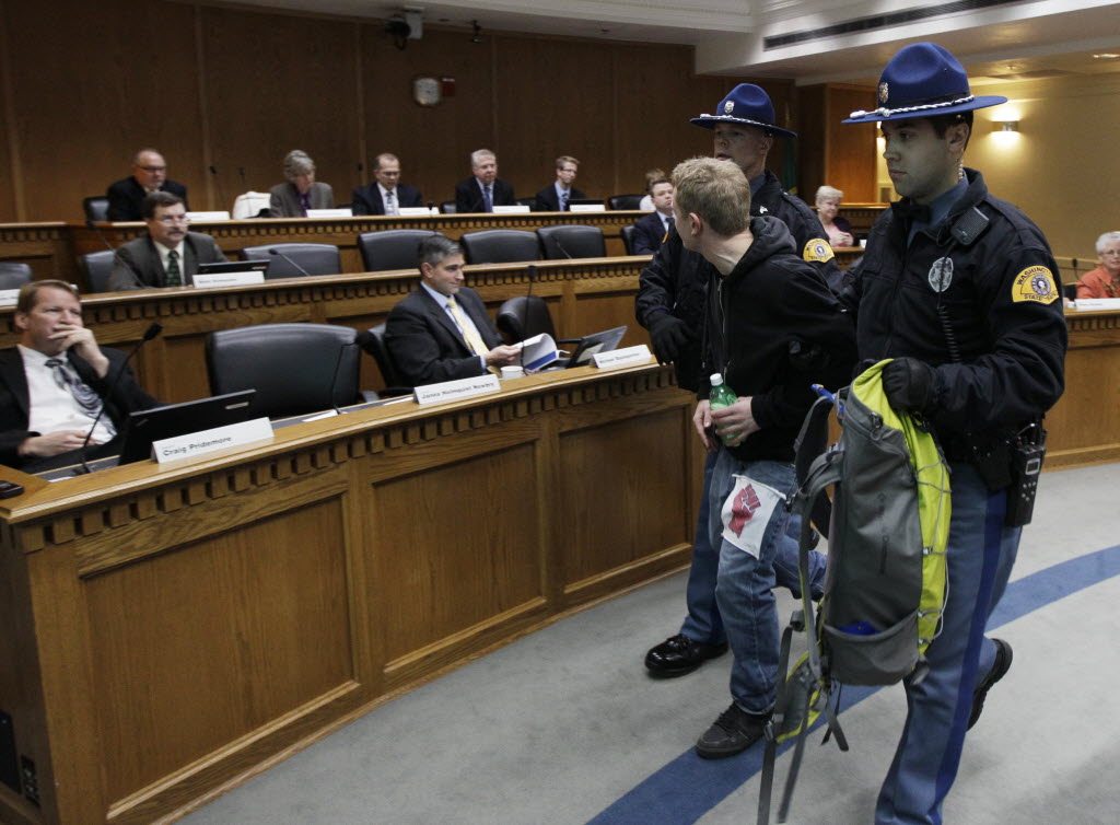 Washington State Patrol troopers remove one of several protesters who disrupted a meeting of the Senate Ways and Means Committee by standing and shouting their opposition to budget cuts at the Capitol in Olympia on Tuesday.