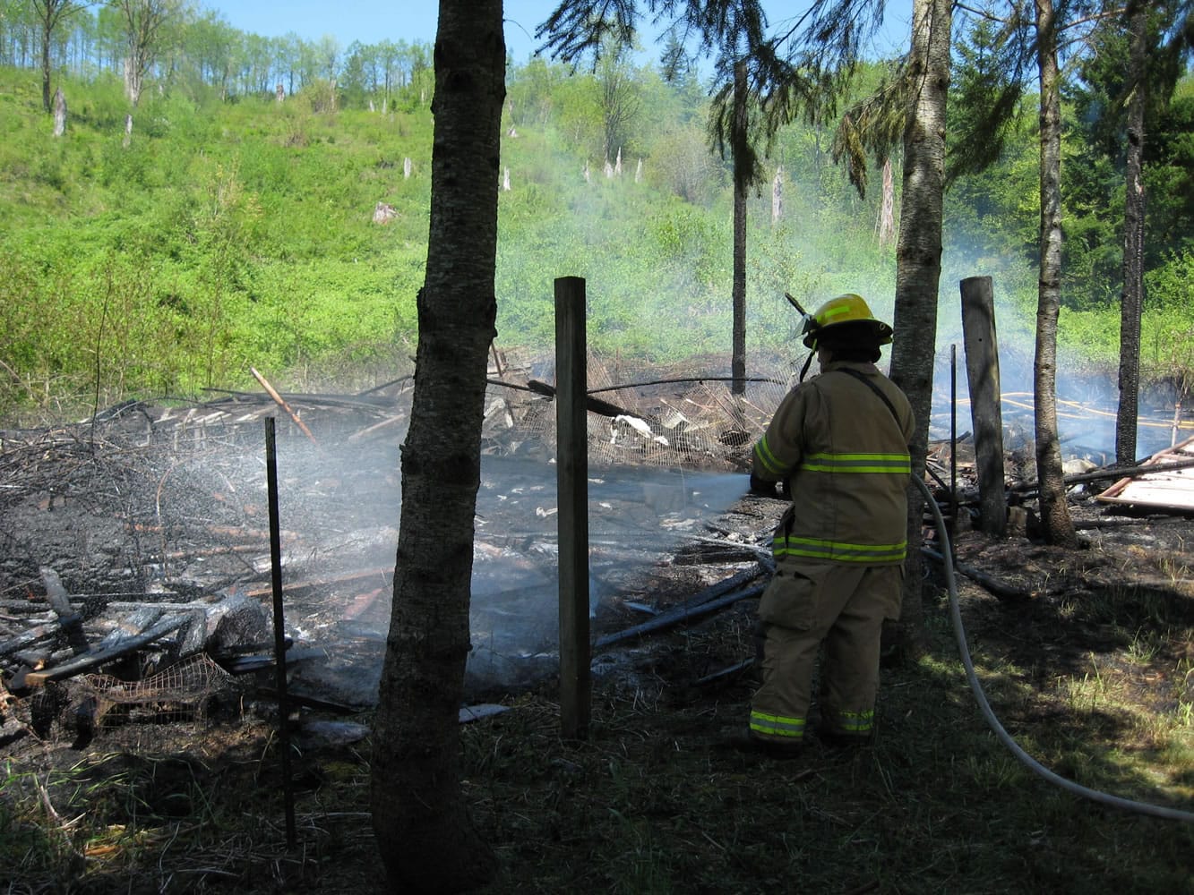 A firefighter sprays down what remains of a barn that burned in a rural area east of Battle Ground on Saturday.