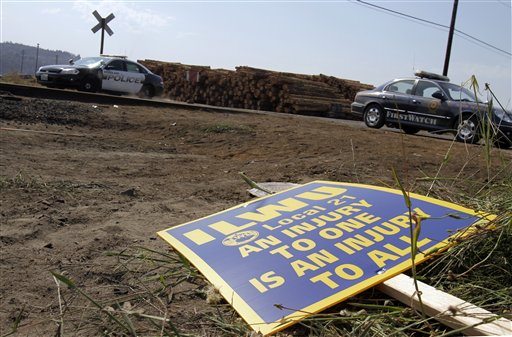 A union sign left from Wednesday's clash between police and union workers is seen in the grass and dirt as police patrol an entrance at the Port of Longview in Longview, Wash., Thursday, Sept. 8, 2011.