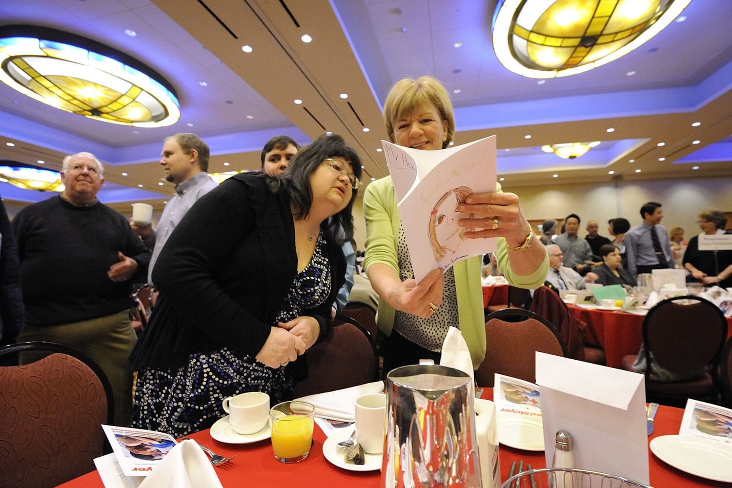Kathy Corwin, right, shares artwork from children about who their heroes are, with Melody Bazzel, who was recognized for her efforts as an animal rescue hero at the 15th annual American Red Cross Real Heroes Breakfast on Friday in Vancouver.