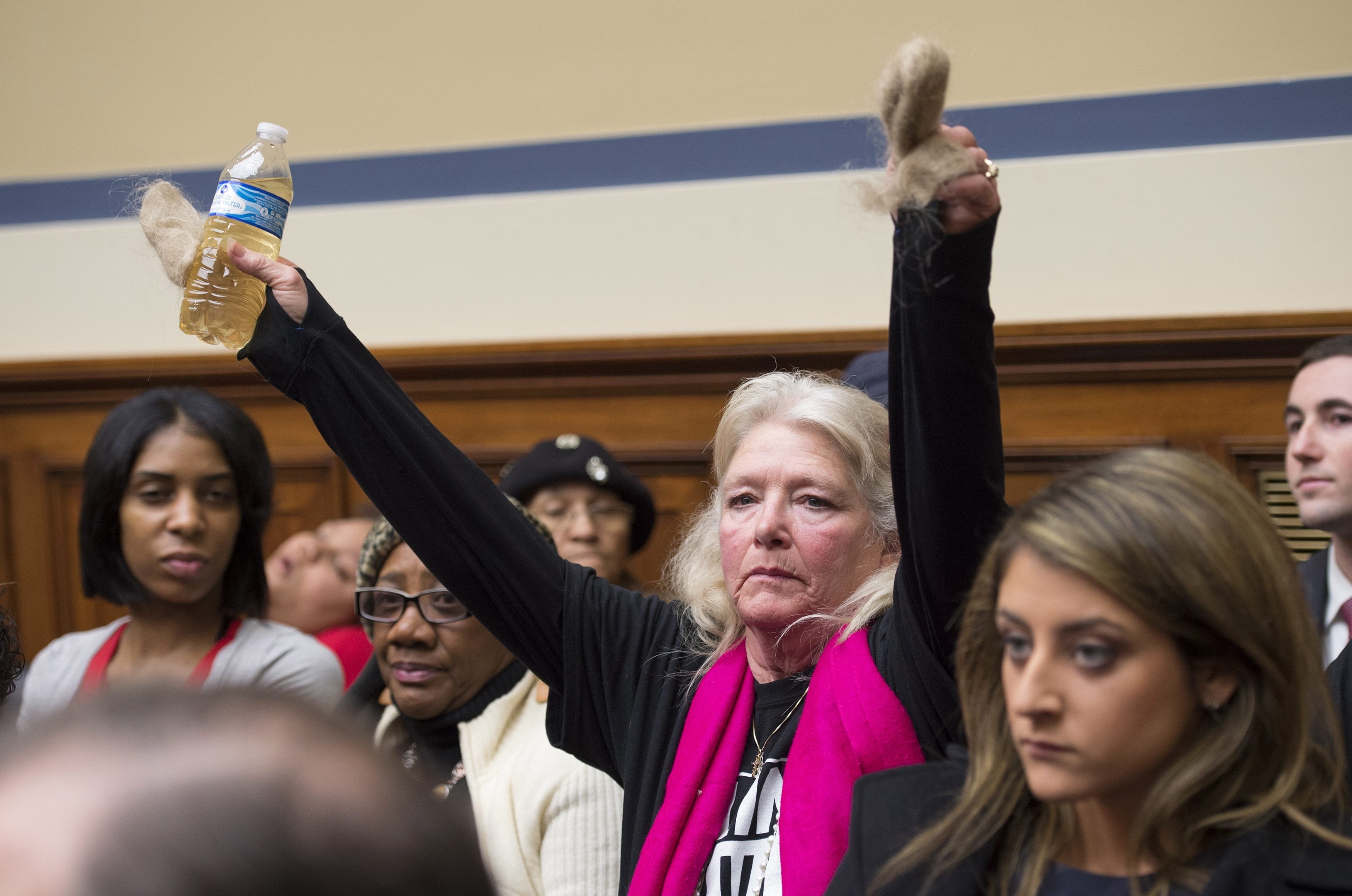 Flint, Mich. resident Glaydes Williamson holds up water from Flint and hair pulled from her drain, during the House Oversight and Government Reform Committee hearing to examine the ongoing situation in Flint, Mich., on Capitol Hill in Washington on Wednesday on Capitol Hill.