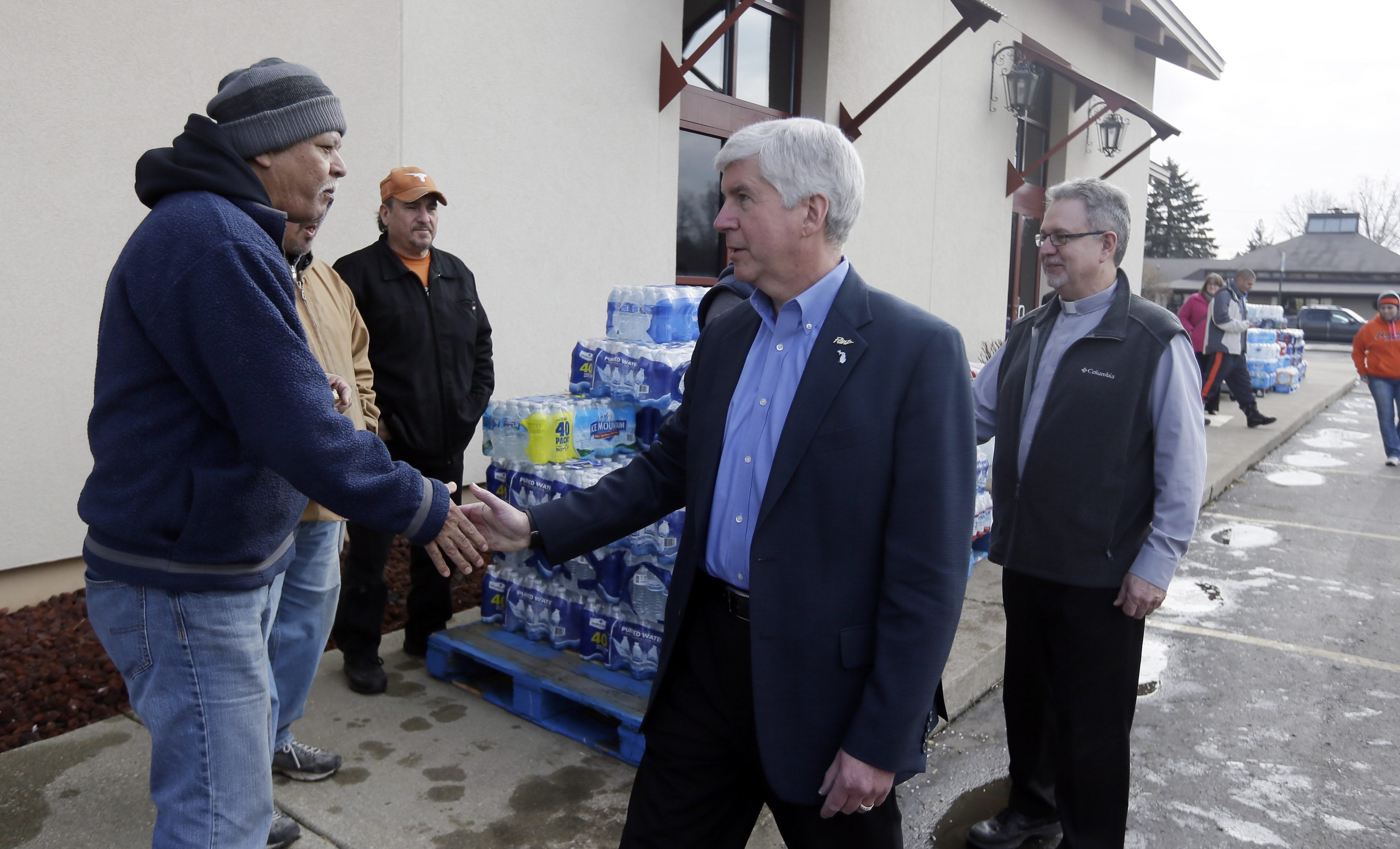 Michigan Gov. Rick Snyder, center and Our Lady of Guadalupe Church Deacon Omar Odette, meets with volunteers helping to load vehicles with bottled water Friday in Flint, Mich. Snyder visited the church that&#039;s distributing water and filters to its predominantly Latino parishioners.