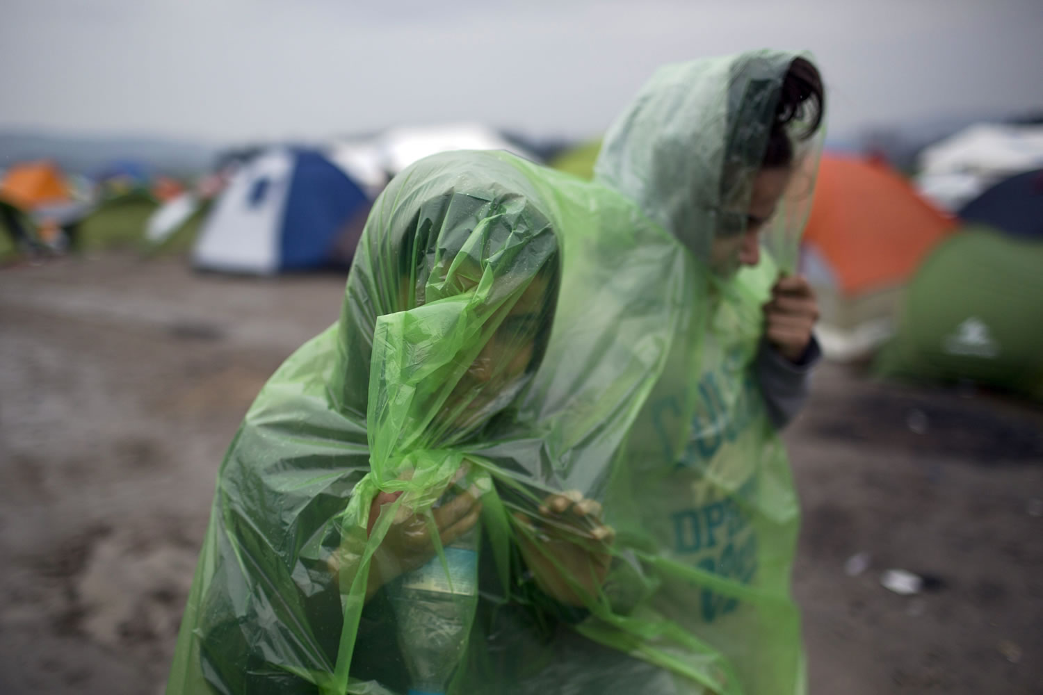 Two girls wearing raincoats walk in front of tents, as refugees wait to be allowed to cross the the Greek-Macedonian border near the northern Greek village of Idomeni , Wednesday, Feb. 24, 2016. The Greek interior ministry said about 12,000 people have been stranded in Greece since neighbor Macedonia began turning Afghan immigrants away at the border and slowing the number of crossings for others heading to central and northern Europe.