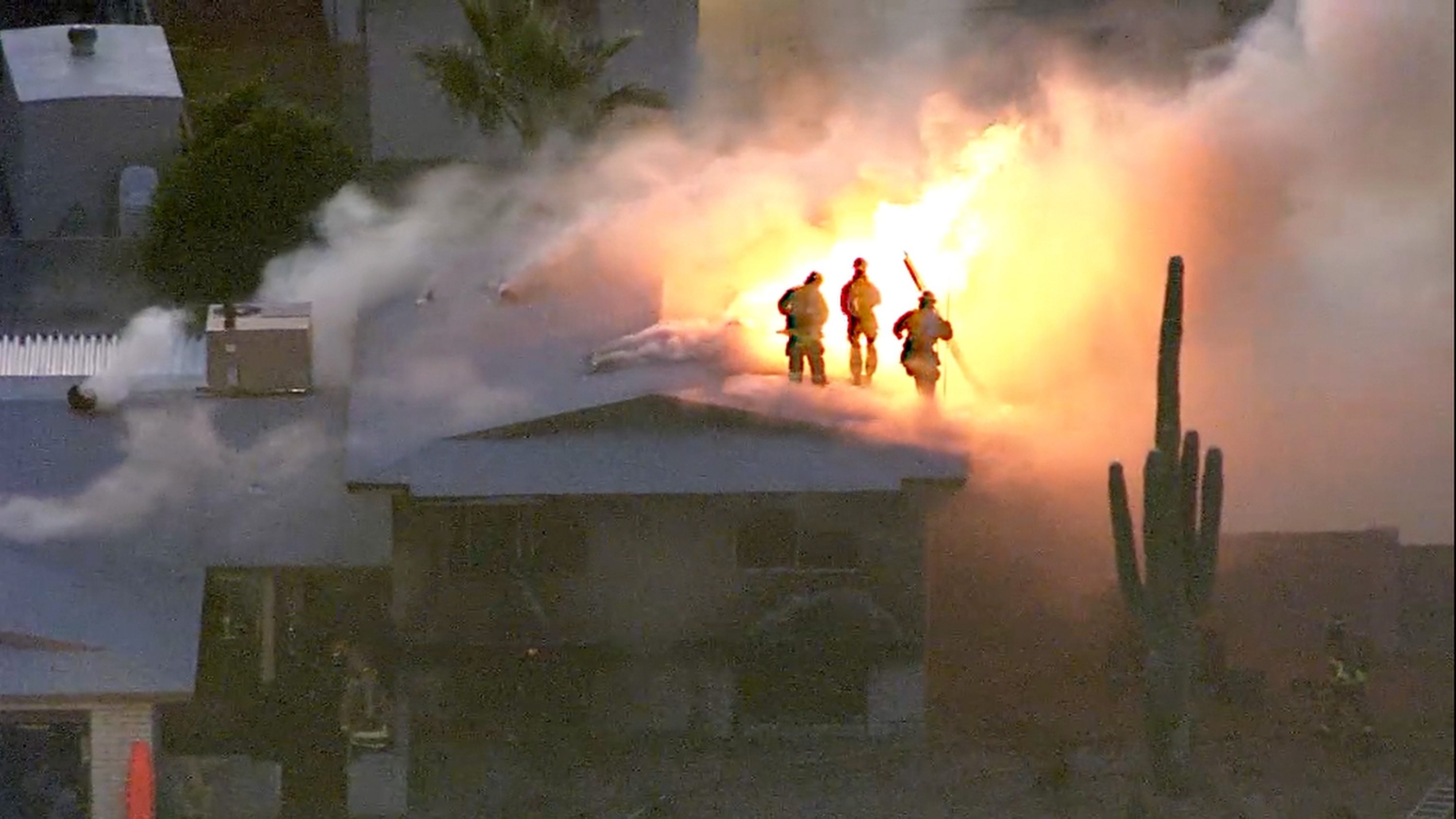 Firefighters atop a house engulfed in flames in Phoenix on Tuesda. Police and firefighters braved bullets and flames as they responded to the fatal shooting and house fire.