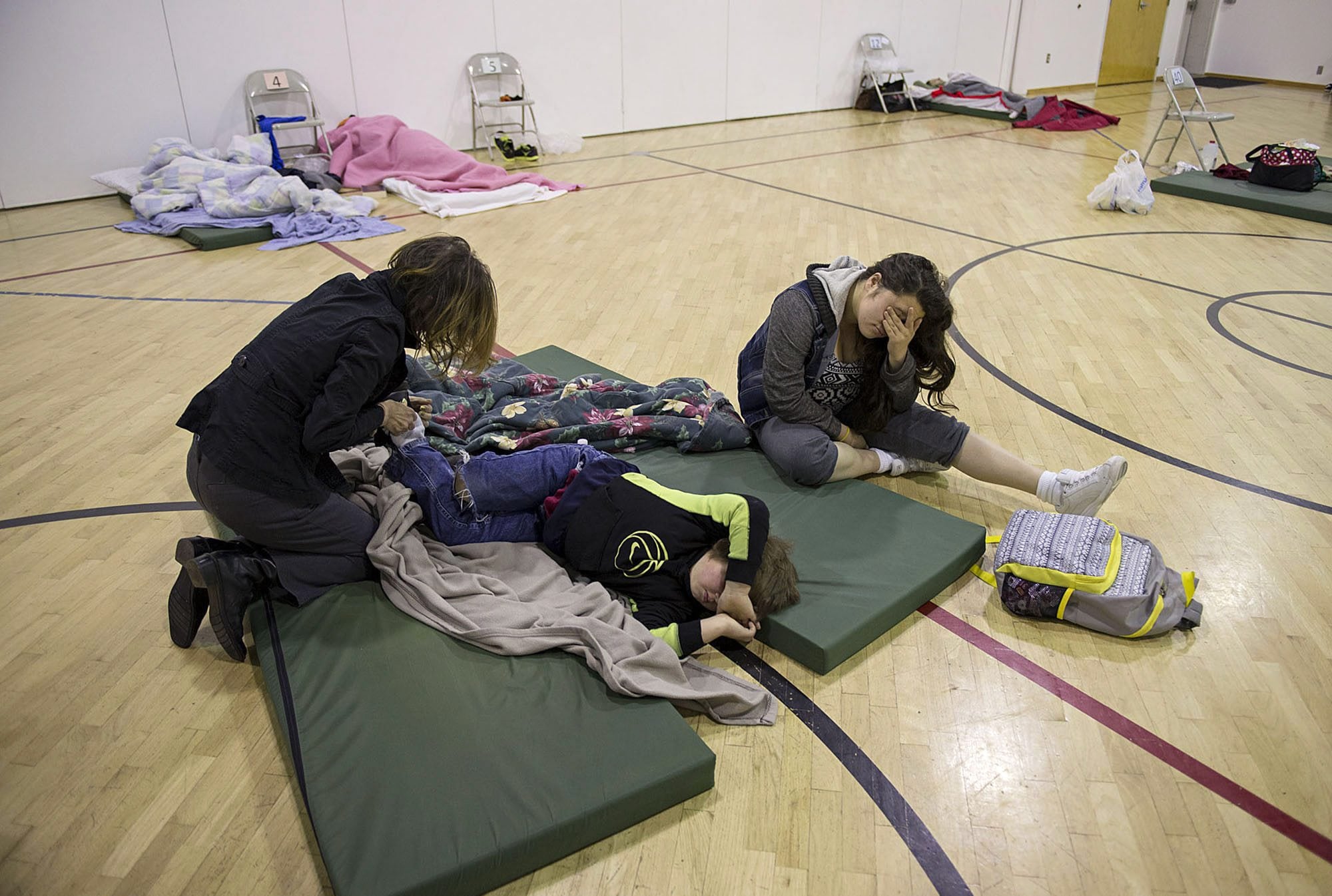 Donna Pinaula, from left, helps wake her kids Johnny Pinaula, 7, and Shyanne Tanguileg, 16, after sleeping all night on the gym floor at St. Andrew Lutheran Church in November as part of the Winter Hospitality Overflow shelter program.