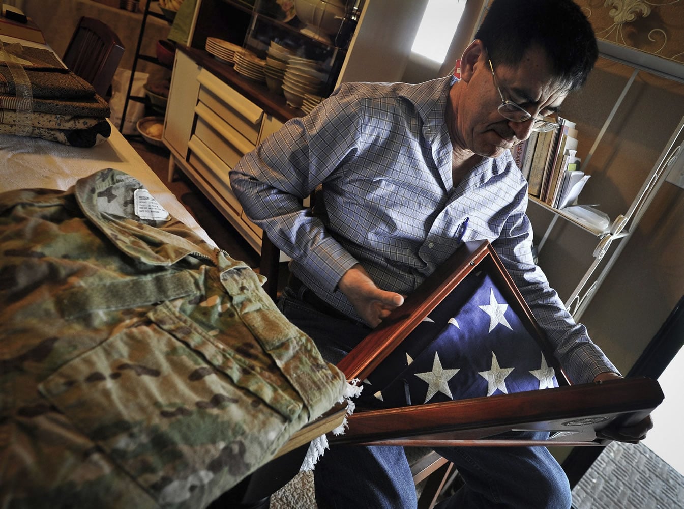 Next to the camouflage uniform of his late son, Army National Guard Spc. Benjamin Pleitez, Salvador Pleitez looks at the flag that draped his casket after he was killed in Mazar-e-Sharif, Afghanistan in 2012.