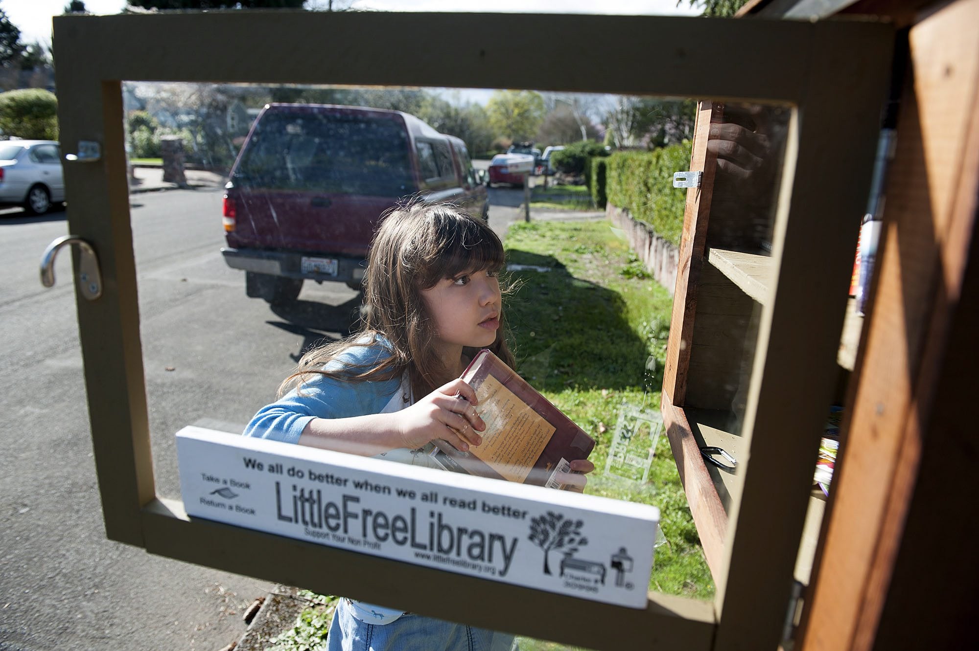 Zoe Chan, 7, adds a donated book to the Clark Avenue Little Free Library. Creating the little library was Zoe&#039;s idea.
