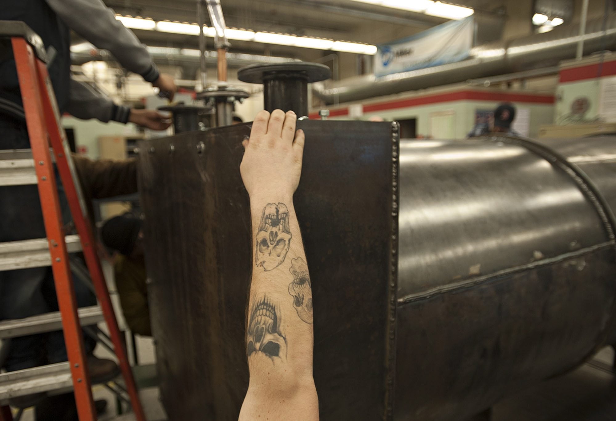 Clark College student David Jeffers stretches his tattooed forearm toward the top of the pressure vessel his class built as he looks for leaks.