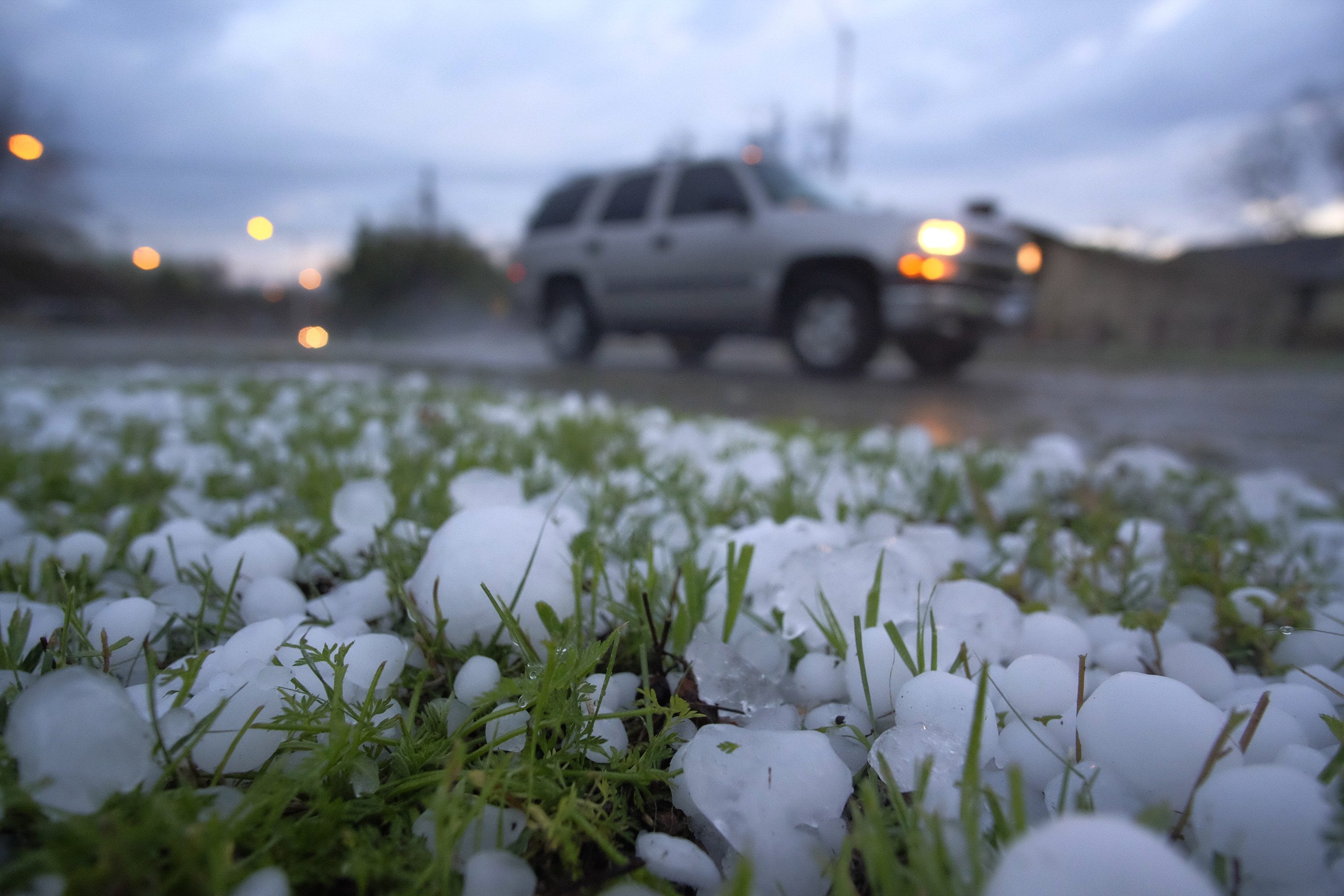 A vehicle drives by a field covered with hail early Thursday in Fort Worth, Texas.