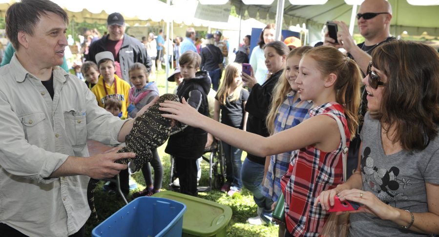 Brett &quot;Mr. Lizard&quot; Wilson, left, introduces a black and white Tegu lizard to Sara Flindt and Jana Flindt, right, during the Earth Day Fest at Salmon Creek Regional Park in Vancouver on Saturday.