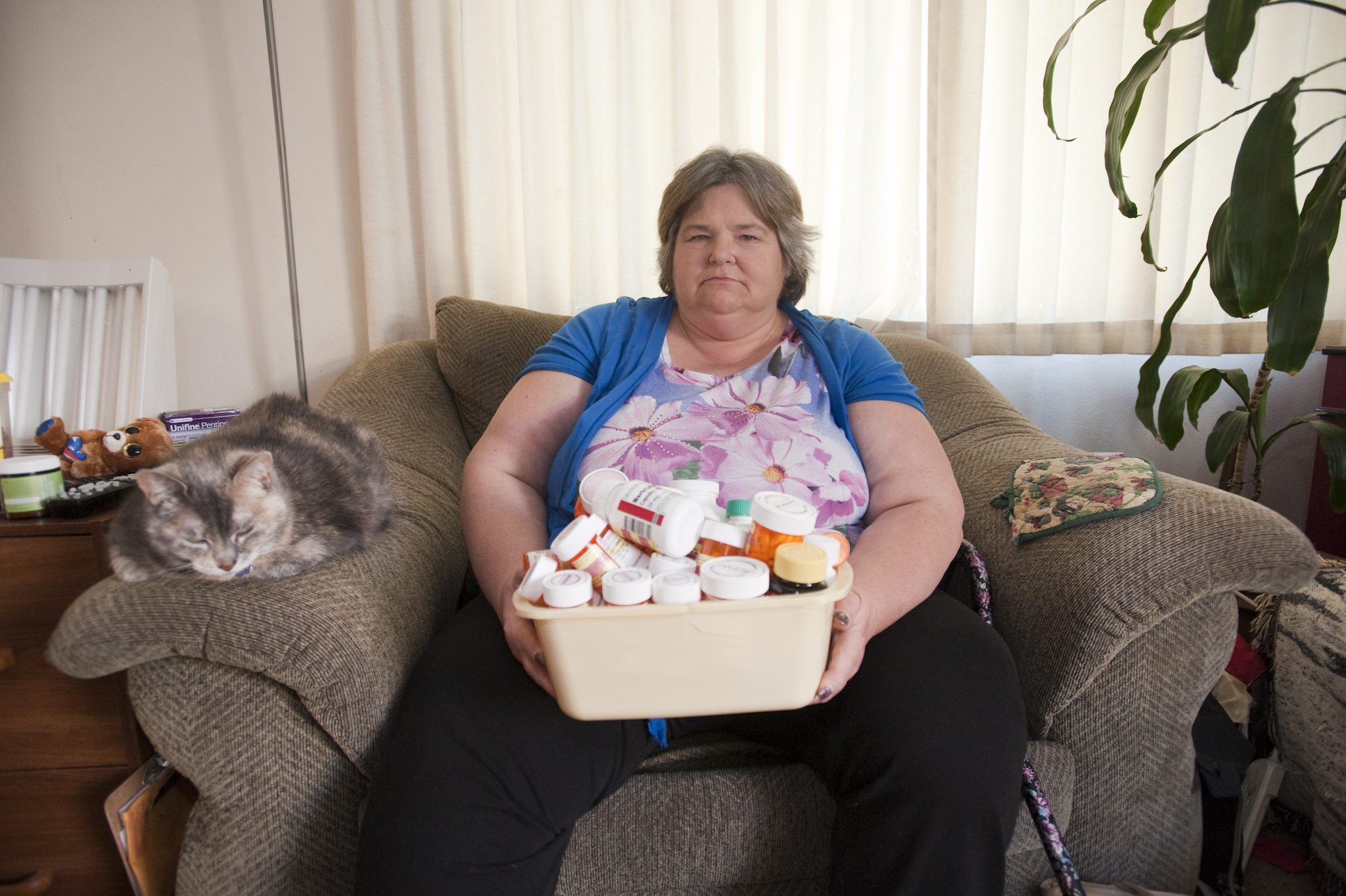 Kay Roberson, at her Vancouver home with her cat Sophie, holds a box of medications she&#039;s been prescribed for diagnosed mental health issues and several chronic health issues. Roberson spent most of her life on Medicaid.