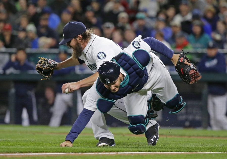 Seattle Mariners starting pitcher Wade Miley, left, reacts as he collides with catcher Chris Iannetta as they try to field a bunt single by Texas Rangers&#039; Delino DeShields during the third inning. (Ted S.