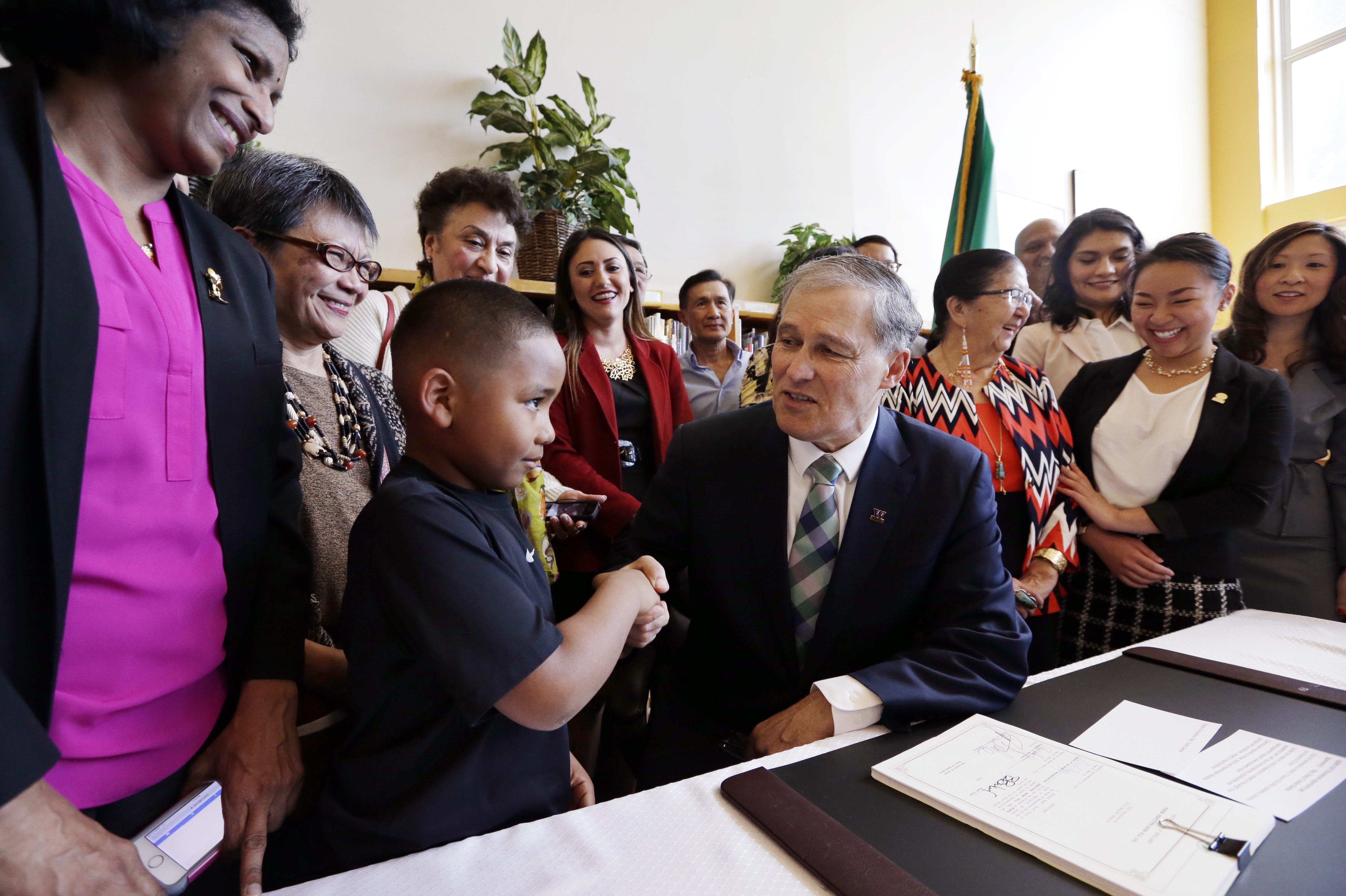 Gov. Jay Inslee shakes hands with a boy as officials stand behind after signing House Bill 1541 at Aki Kurose Middle School on Wednesday in Seattle. Inslee signed the bill aimed at closing the so-called opportunity gaps faced by kids from low-income and minority families.