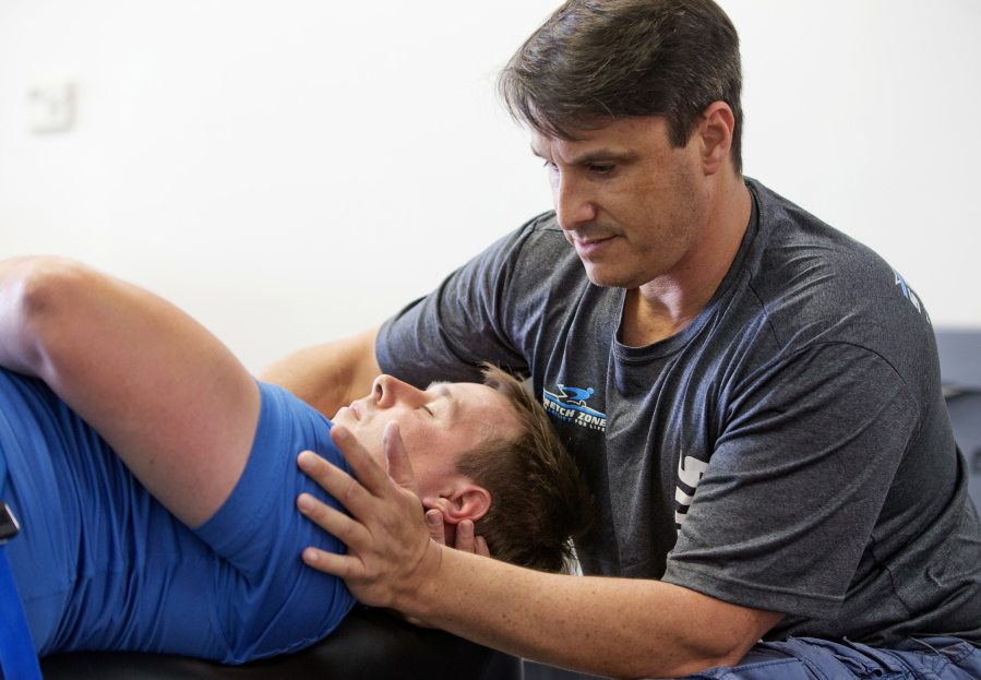 In this March 17, 2016 photo, Jorden Gold, right, founder and CSO of Stretch Zone, demonstrates stretching techniques on Neill Broome, vice president of operations for the company in Boca Raton, Fla. Most CrossFit and similar high intensity workouts, that have become more frequent with increasing popularity, are not meant for average gym-goers, said Gold, who founded Stretch Zone. During the 30-minute sessions, therapists use bolsters and belts to stretch clients on a table from angles that are nearly impossible to stretch on one?s own.