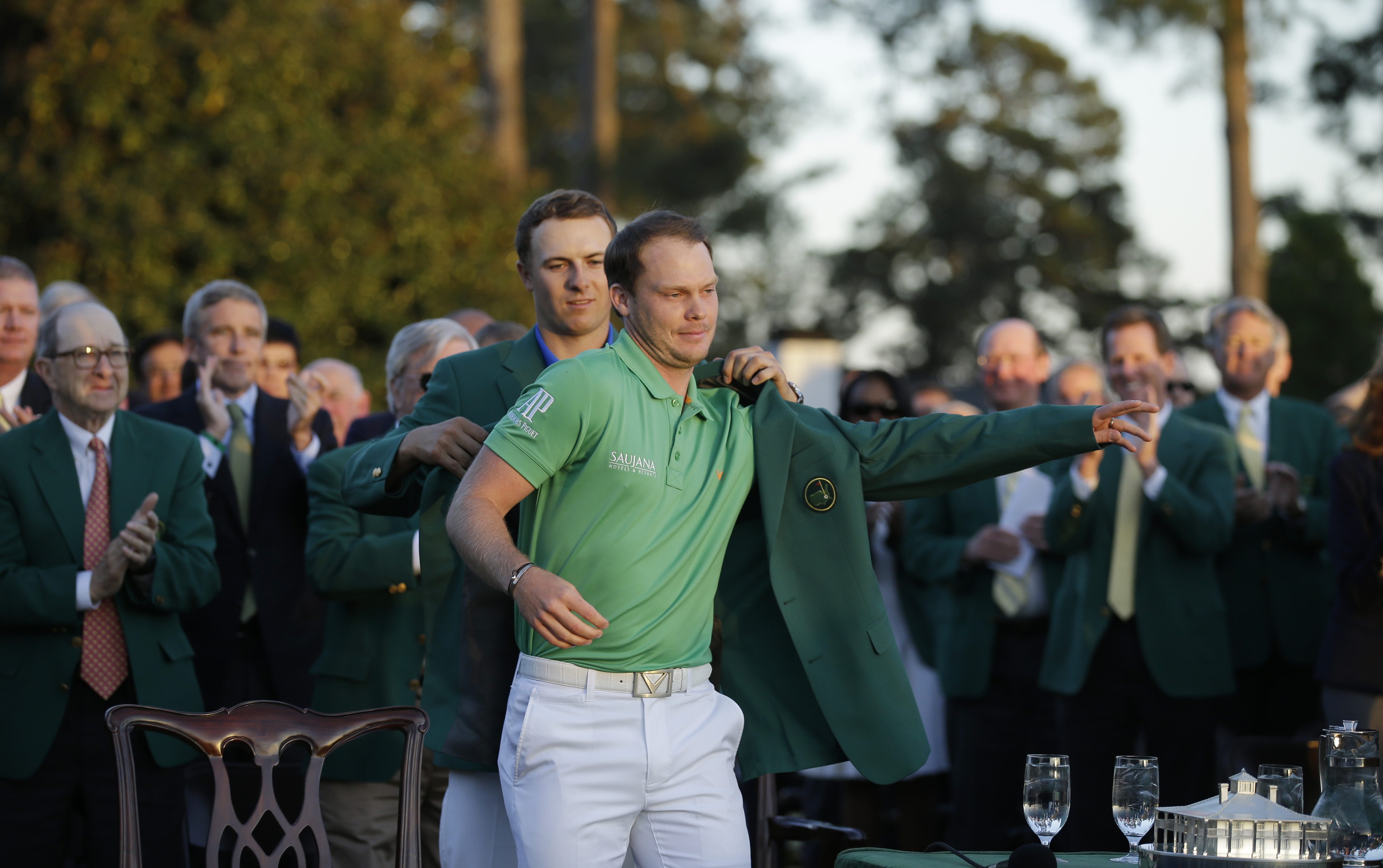 Defending champion Jordan Spieth, left, helps 2016 Masters champion Danny Willett, of England, put on his green jacket following the final round of the Masters golf tournament Sunday, April 10, 2016, in Augusta, Ga.