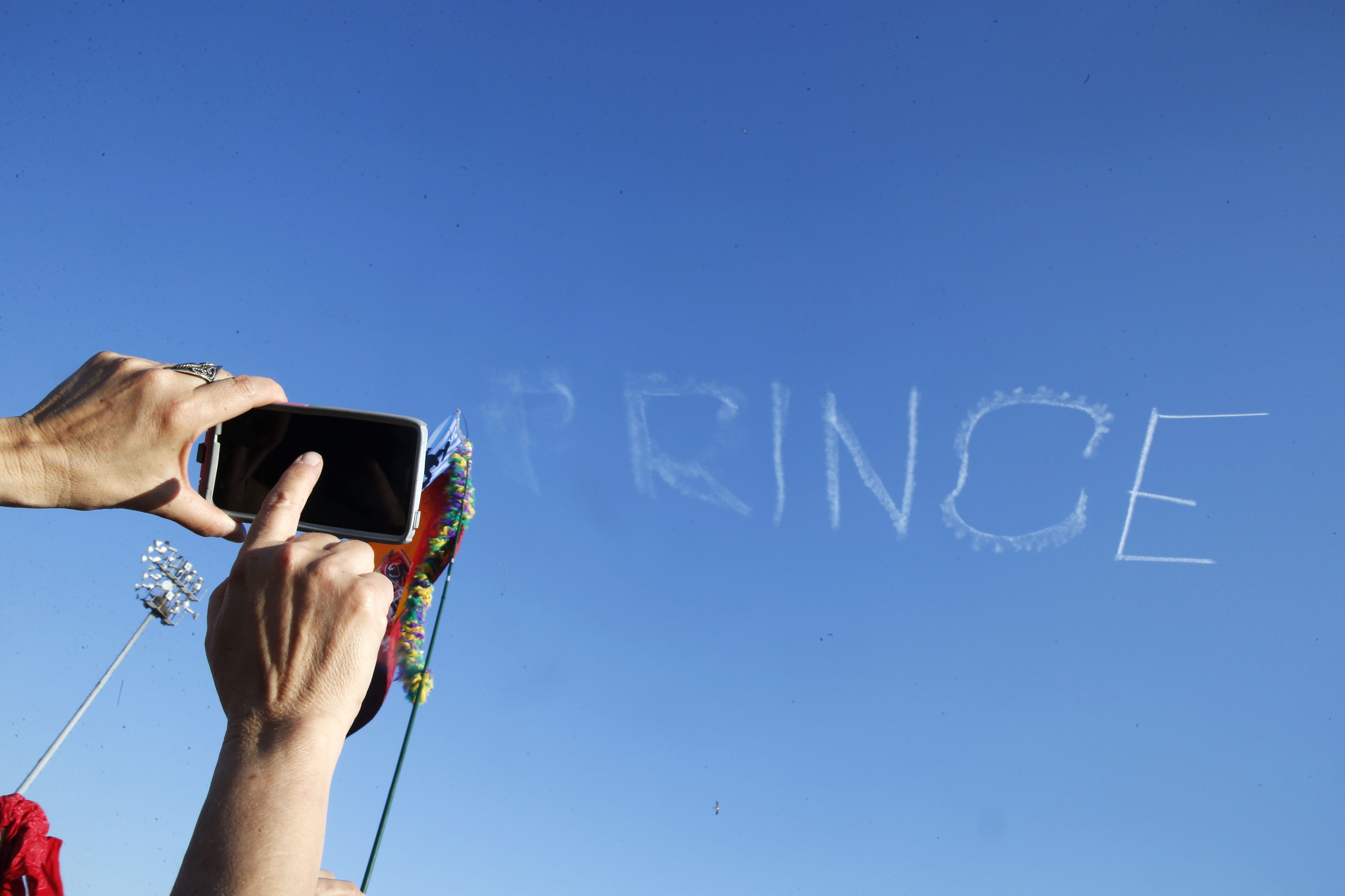 A festival-goer takes a photo as a skywriter spells "Prince," in honor of pop music icon Prince, at the New Orleans Jazz and Heritage Festival in New Orleans, Saturday, April 23, 2016. Prince died Thursday at the age of 57.