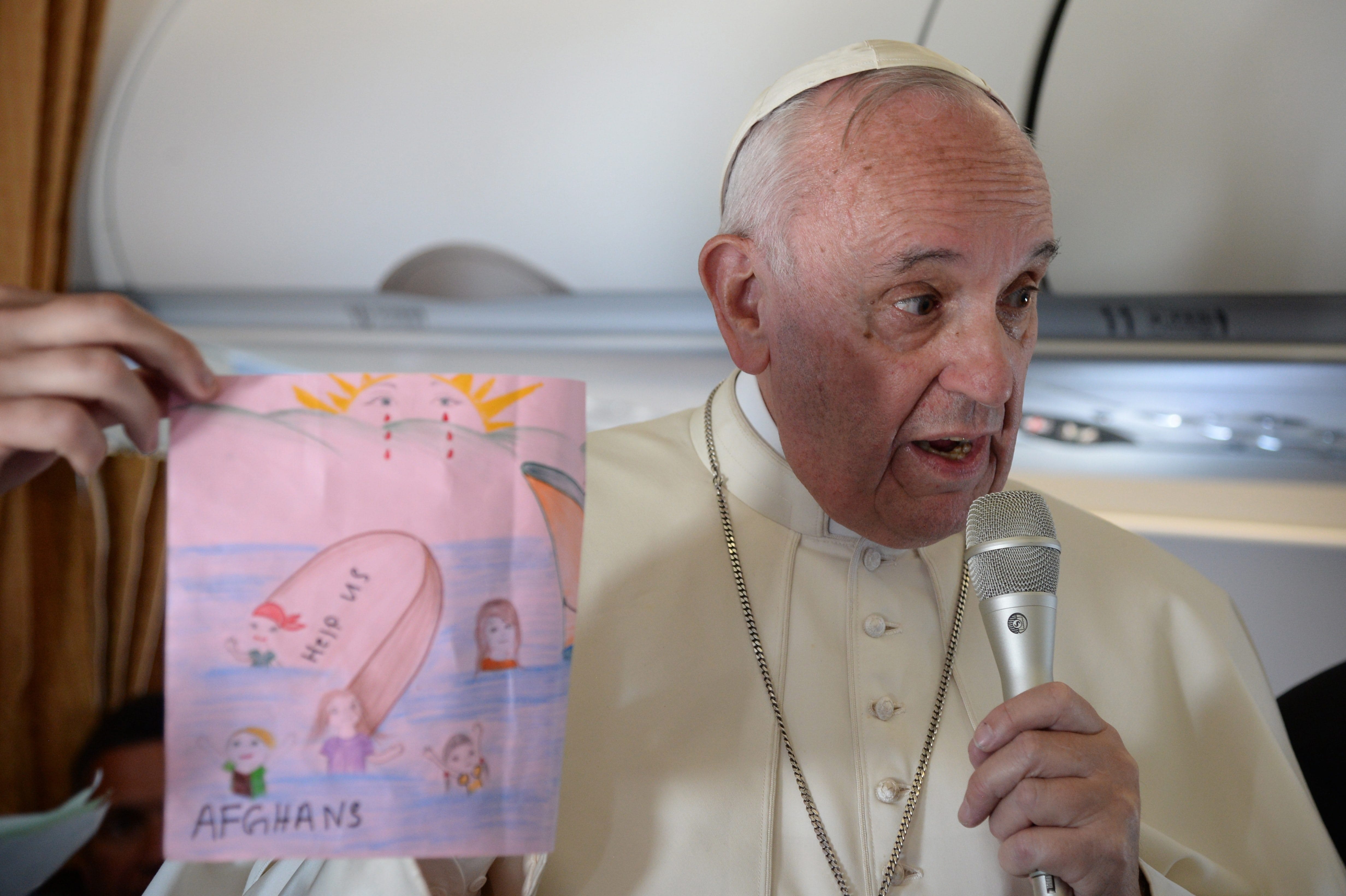 Pope Francis shows drawings made by children on his flight back to Rome following a visit to the Greek island of Lesbos, Saturday, April 16, 2016. Pope Francis gave Europe a provocative and concrete lesson in how to treat refugees Saturday by bringing home 12 Syrian Muslims aboard his charter plane after an emotional visit to the hard-hit Greek island of Lesbos.