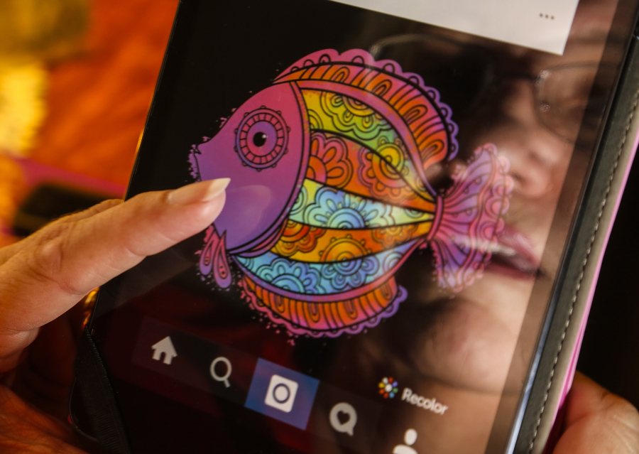 Long Beach resident Cheri Brown is reflected on the screen of her iPad Mini, on which she makes vibrant graphic designs using the coloring app Recolor.