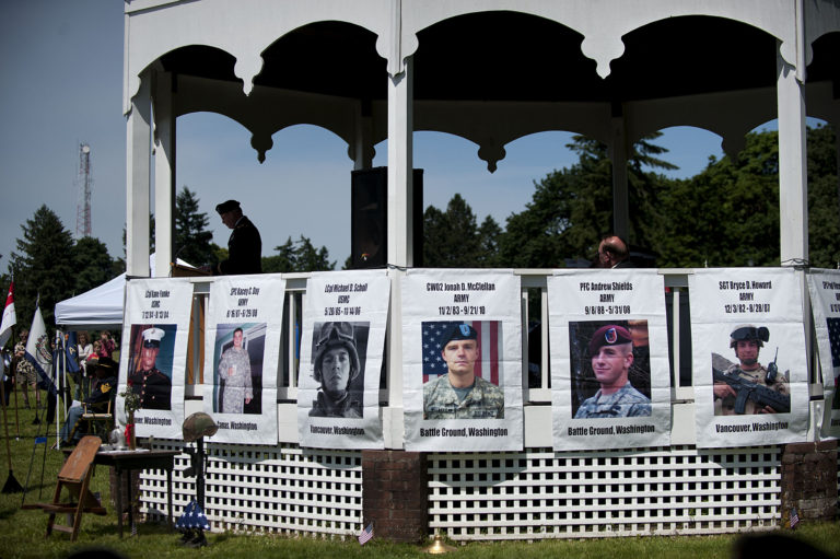 Photos of local heroes who died in combat are displayed as Col. John Sweeney speaks to the crowd during Vancouver's Memorial Day Observance on Monday morning, May 30, 2016 at Fort Vancouver National Historic Site.