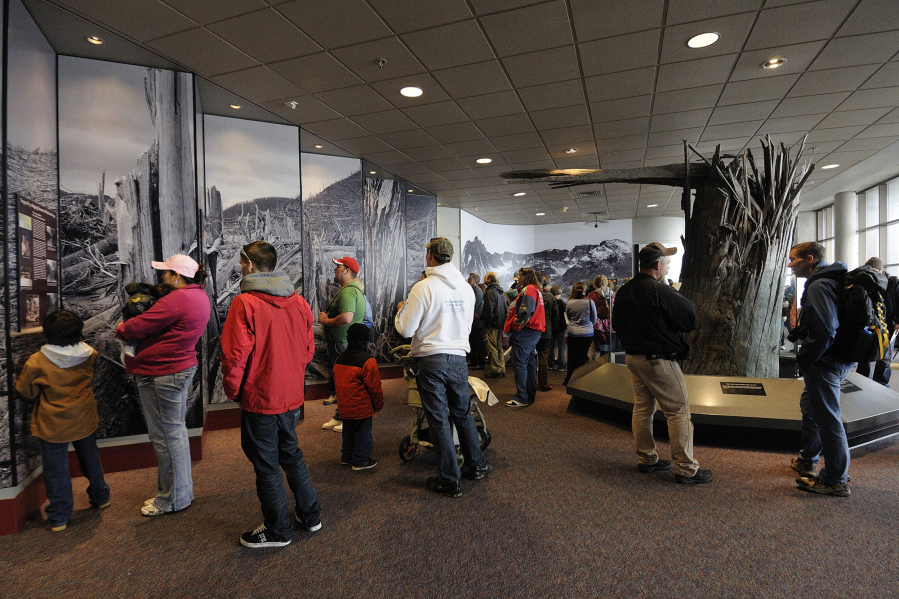 Visitors read about Mount St. Helens near a display of an old-growth tree stump blown over by the volcanic eruption of Mount St. Helens.
