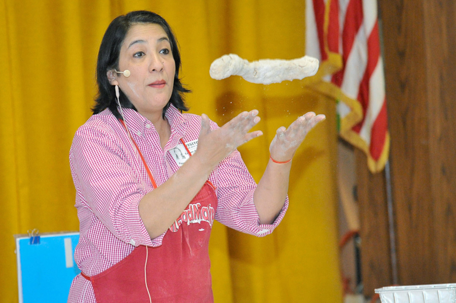 Esther Arce-Reed demonstrates how to toss the dough made during a bread-making demonstration that she and her husband turn into lessons in math and science.